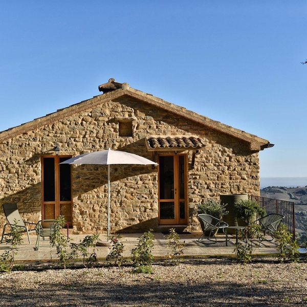 Refugium Hideaways, a restored stone cottage with a terrace and parasol overlooking rolling Italian hills