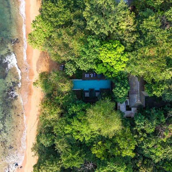 Aerial view of a Príncipe Collection villa with a private pool in tropical forest beside a sandy beach